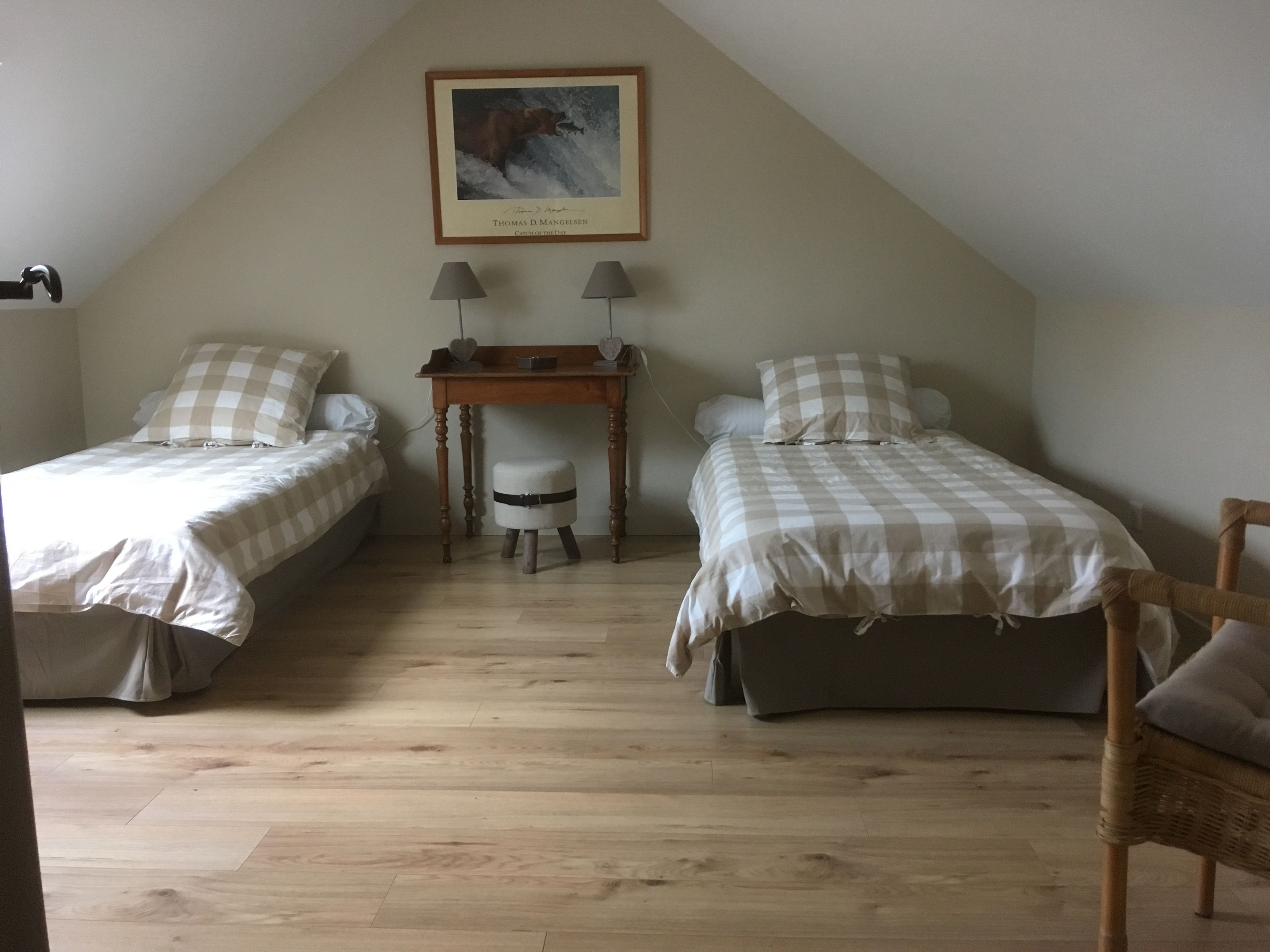 A bedroom with two single beds, a small table, and a chair.