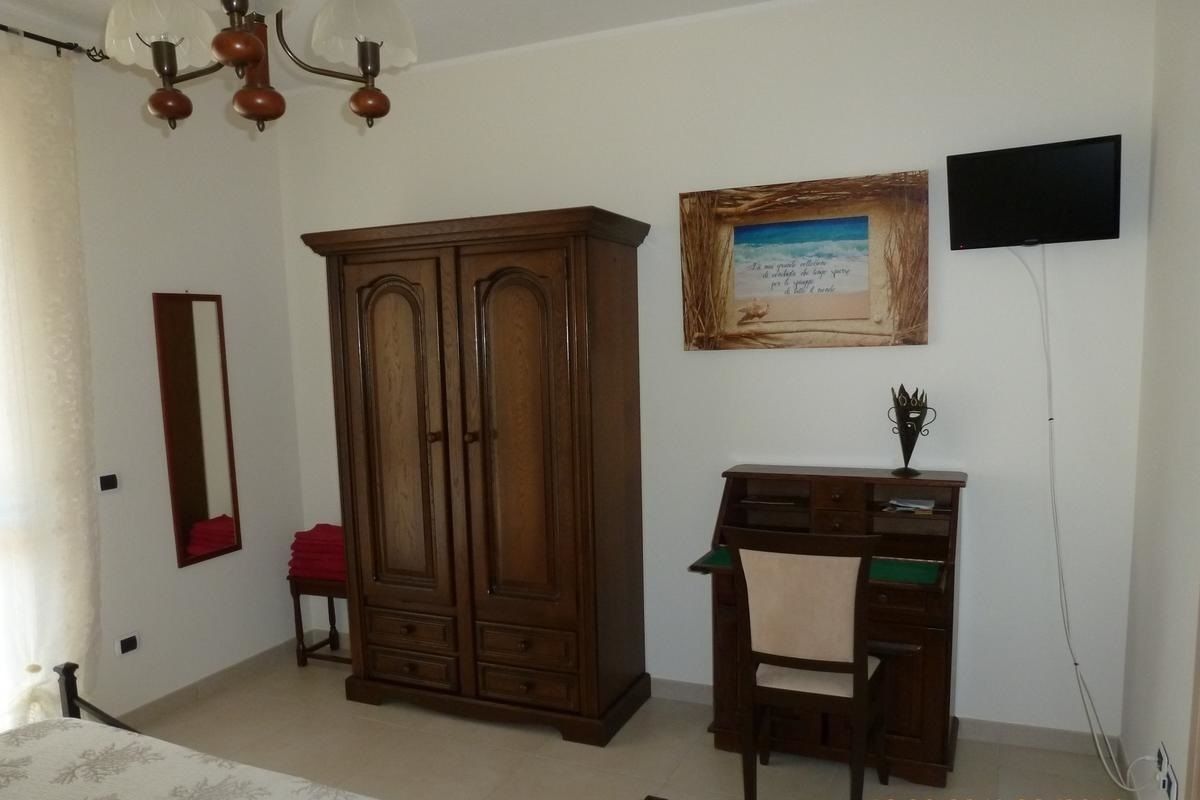 A bedroom with a bed, a wardrobe, a desk, and a television mounted on the wall.