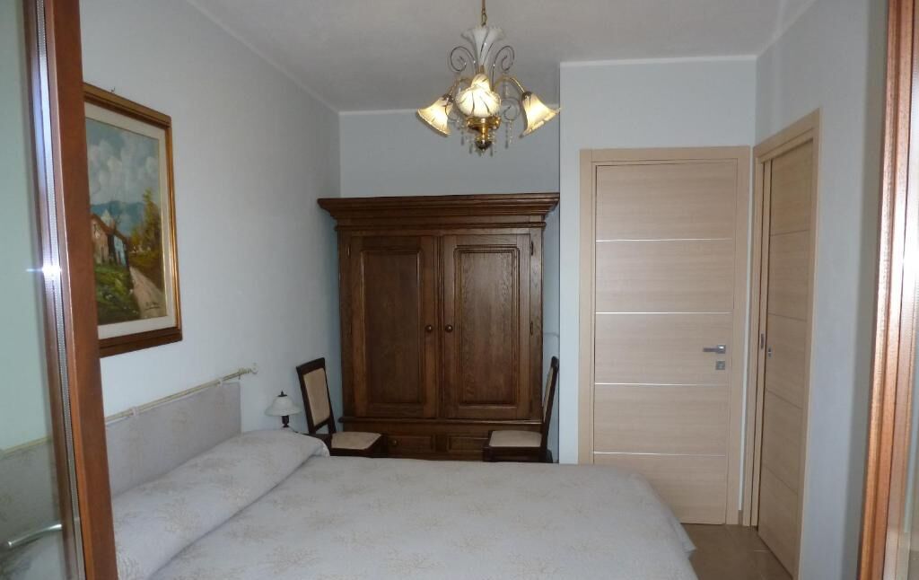 A bedroom with a bed, a wooden wardrobe, a chandelier, and a door.