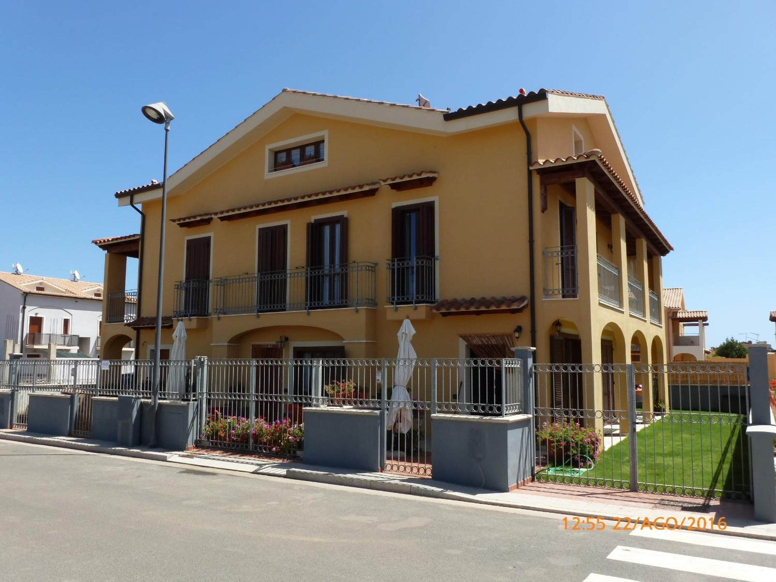A two-story building with a yellow facade, balconies, and a gated entrance.