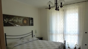 A bedroom with a bed, a nightstand, a chandelier, and a large window with curtains. - Sogno di Mare (Pula)