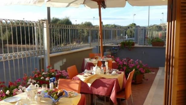 An outdoor dining area with tables set for two, covered by umbrellas, and surrounded by potted plants. - Sogno di Mare (Pula)