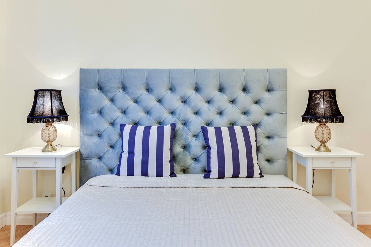 A bedroom with a tufted headboard, two bedside tables, and striped pillows.