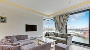 A modern living room with a large window, a flat-screen TV, and a sofa set. - Navy Group - Old Town Apartments (Gdansk)