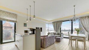 A modern living room with a kitchen area, a dining table, and a large window with a view of the city. - Navy Group - Old Town Apartments (Gdansk)