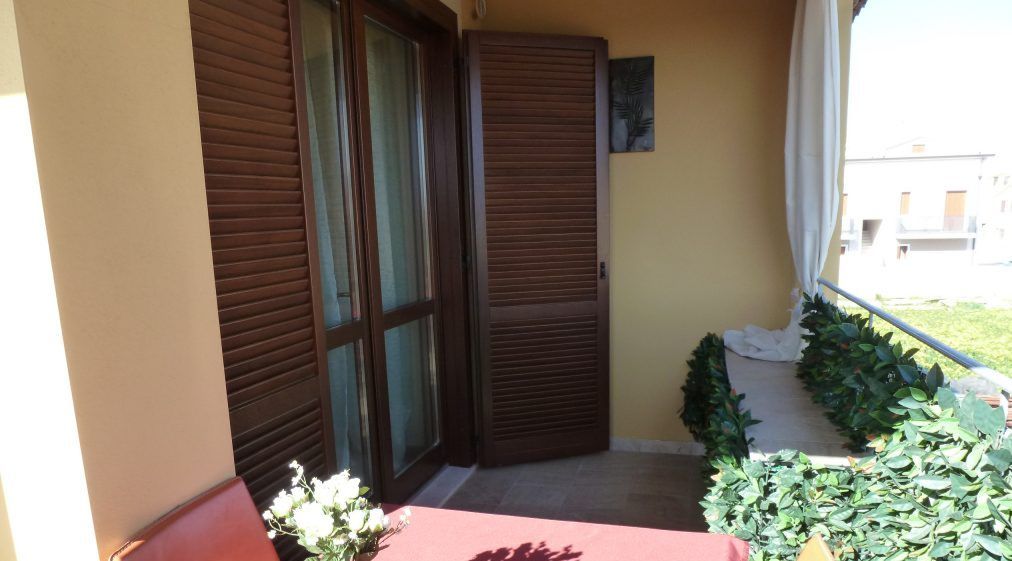 A balcony with a red table, a brown door, and a small garden area with plants.