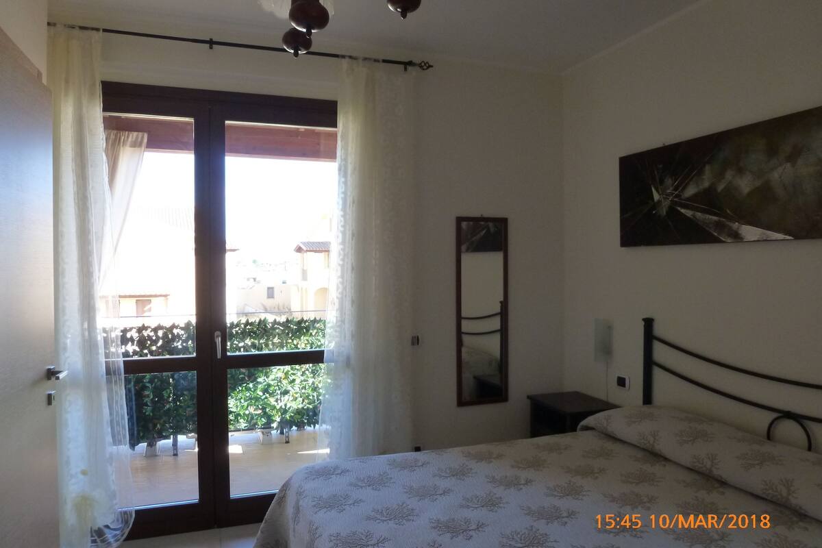 A bedroom with a bed, a window with curtains, a painting on the wall, and a date stamp.