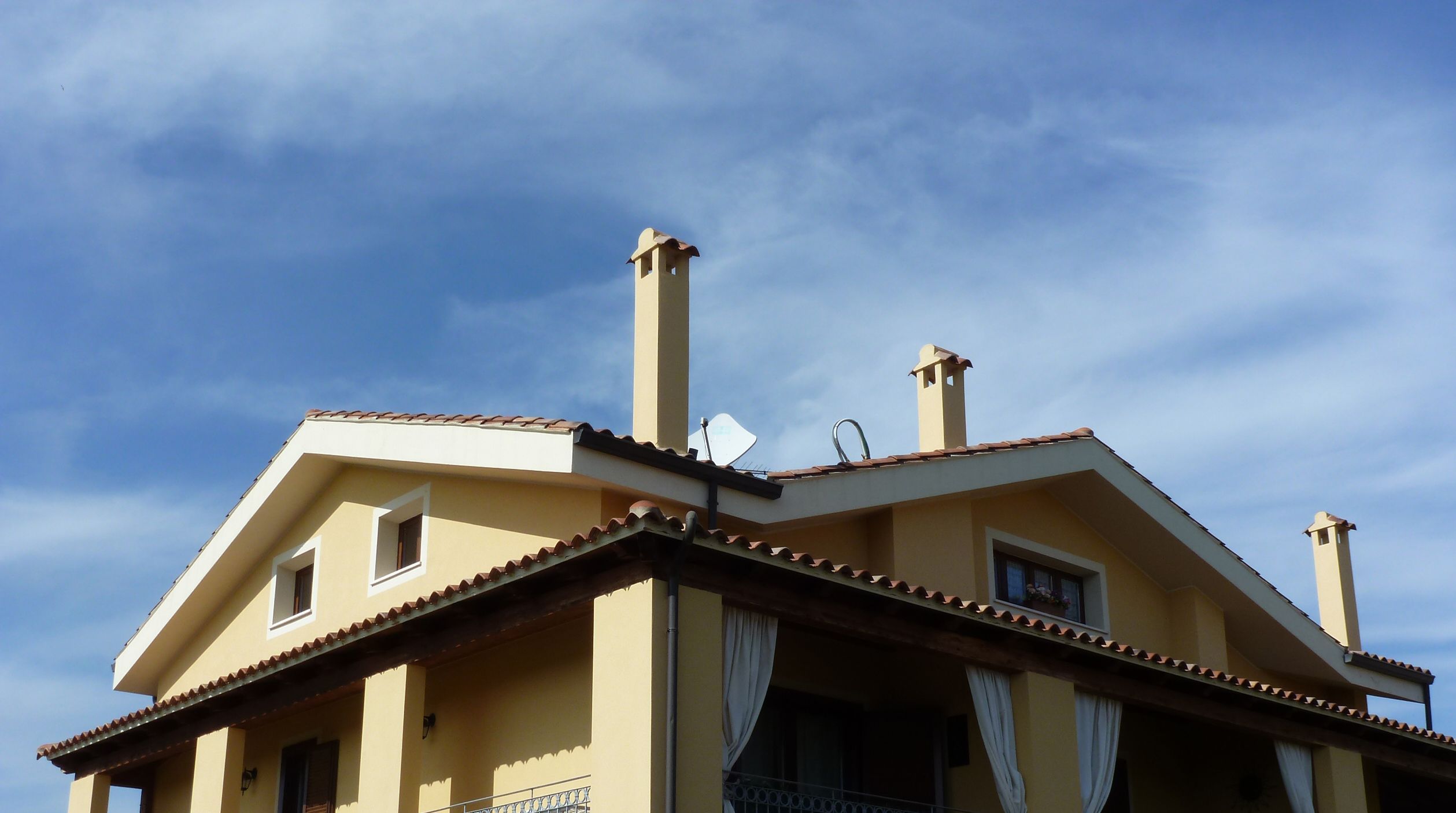 A building with a yellow facade, multiple chimneys, and a tiled roof.