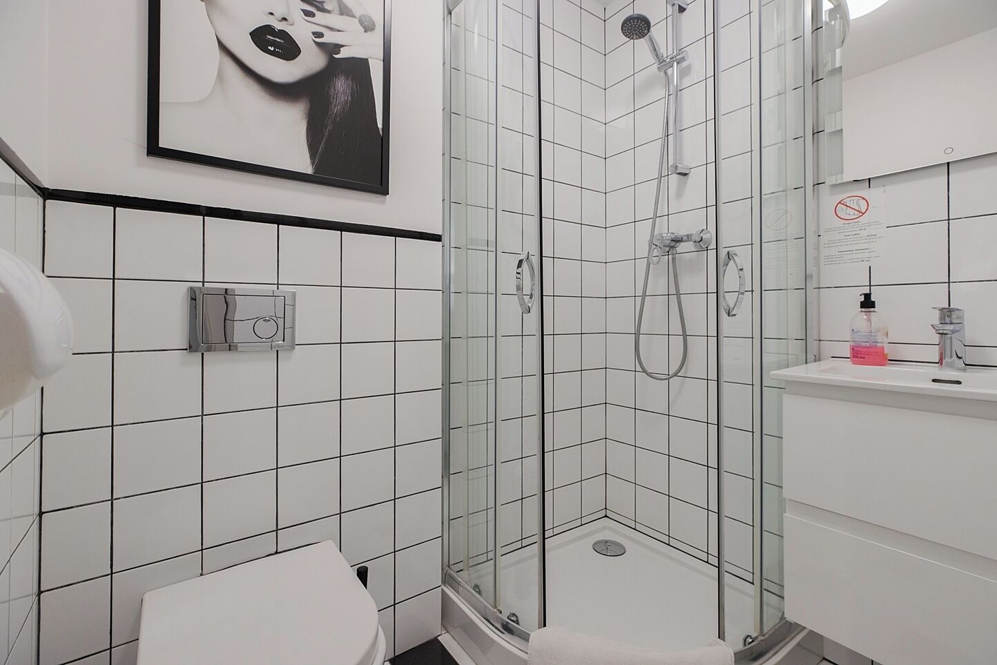 Uma casa de banho moderna com cabine de duche em vidro, paredes revestidas de azulejos brancos, sanita e lavatório com espelho.