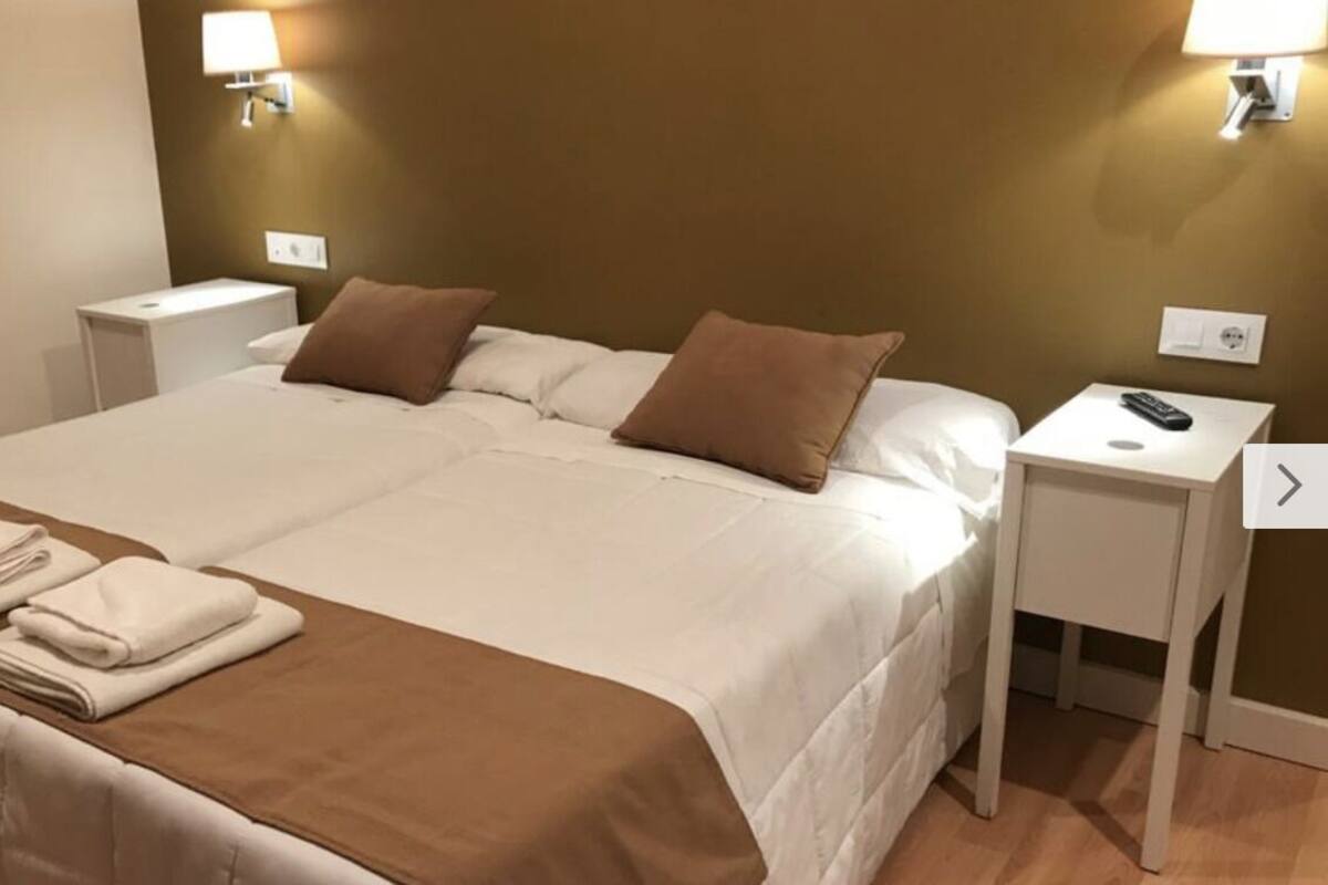 Een tweepersoonsbed met een bruin hoofdbord, wit beddengoed en twee nachtkastjes met lampen.