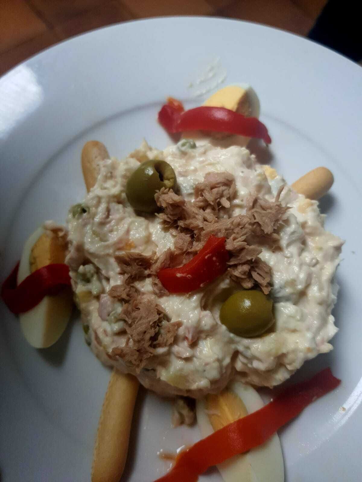A plate with a creamy dish topped with shredded meat, olives, and red bell pepper strips.