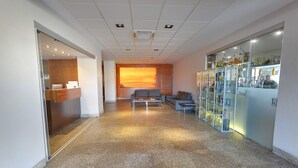 A modern lobby with a reception desk, seating area, and a display of products. - Hotel Moya (Navalmoral de la Mata)