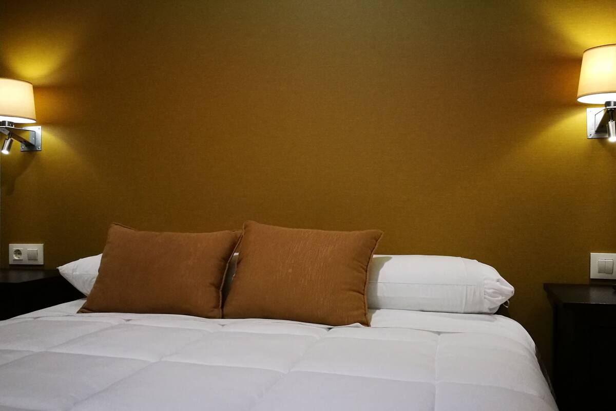 Een hotelkamer met een bed, twee nachtkastjes en wandlampen.