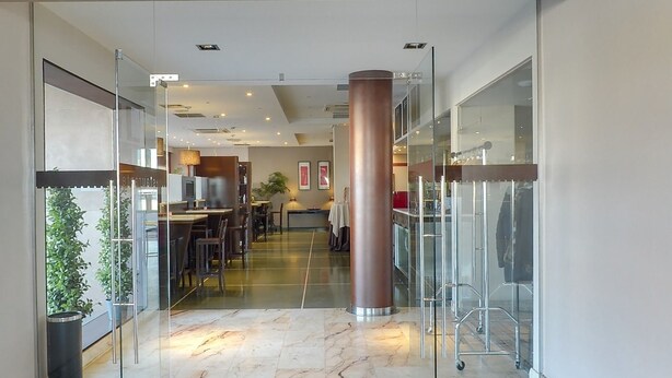 A modern hotel lobby with glass doors, a central pillar, and a seating area with tables and chairs. - Hotel Moya (Navalmoral de la Mata)