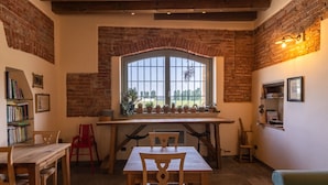 A cozy dining area with a brick wall, a large window, and a wooden table with chairs. - Agriturismo Cascina Pezzolo (Pieve Fissiraga)