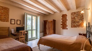 A bedroom with two beds, a desk with a computer, a chair, and a brick wall. - Agriturismo Cascina Pezzolo (Pieve Fissiraga)