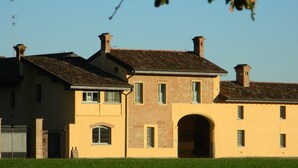 A large, two-story building with a symmetrical facade, featuring a central arched doorway and multiple windows. - Agriturismo Cascina Pezzolo (Pieve Fissiraga)