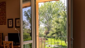 An open sliding door leading to a balcony with a view of a garden and trees. - Agriturismo Cascina Pezzolo (Pieve Fissiraga)