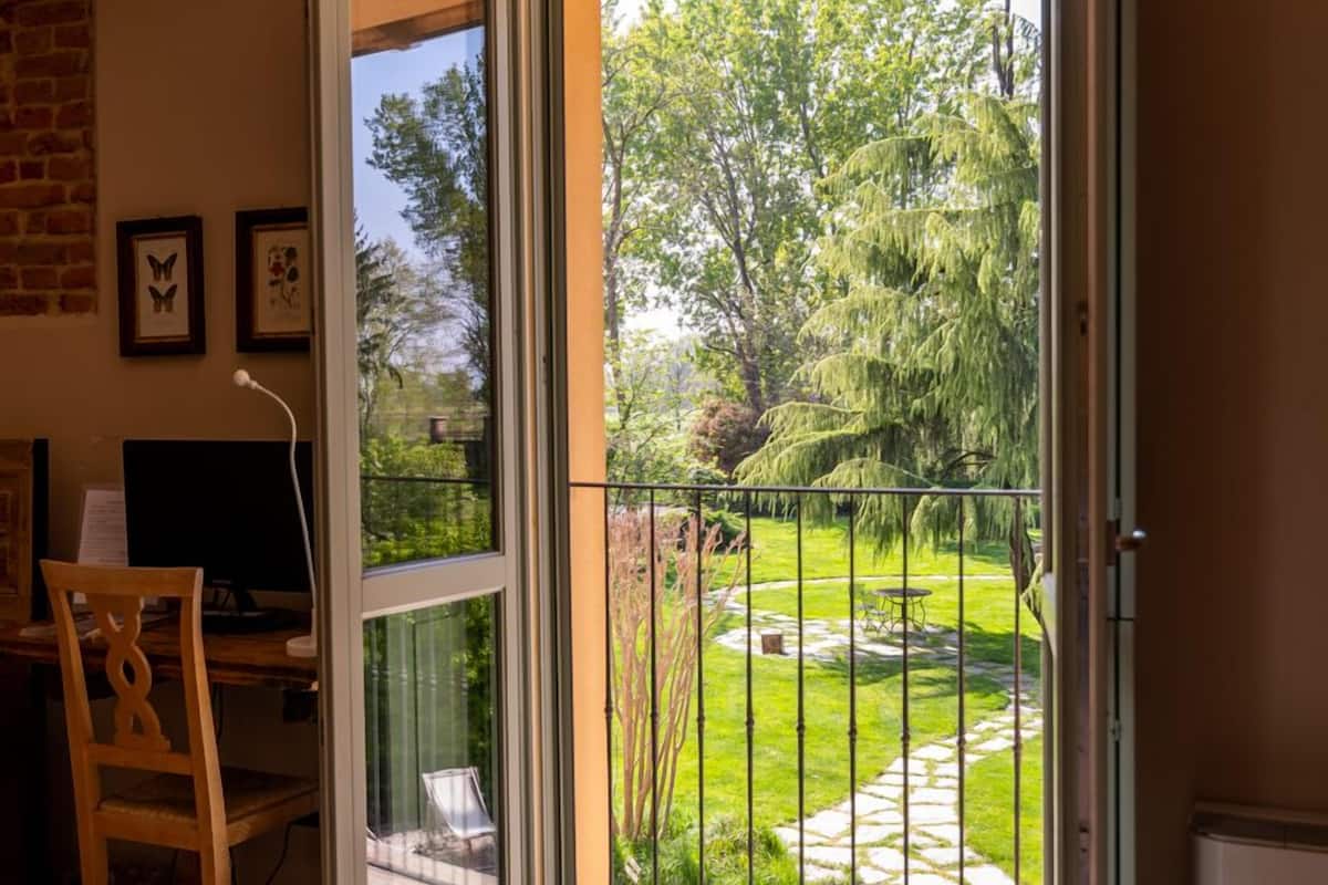 An open sliding door leading to a balcony with a view of a garden and trees.