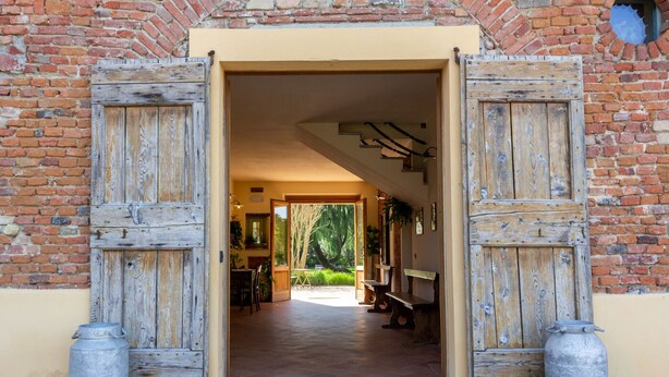 A rustic entrance with wooden doors leading to an interior with a dining area and benches. - Agriturismo Cascina Pezzolo (Pieve Fissiraga)