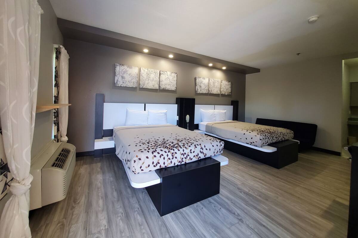 A modern hotel room with two beds, a built-in air conditioner, and a large window with curtains.