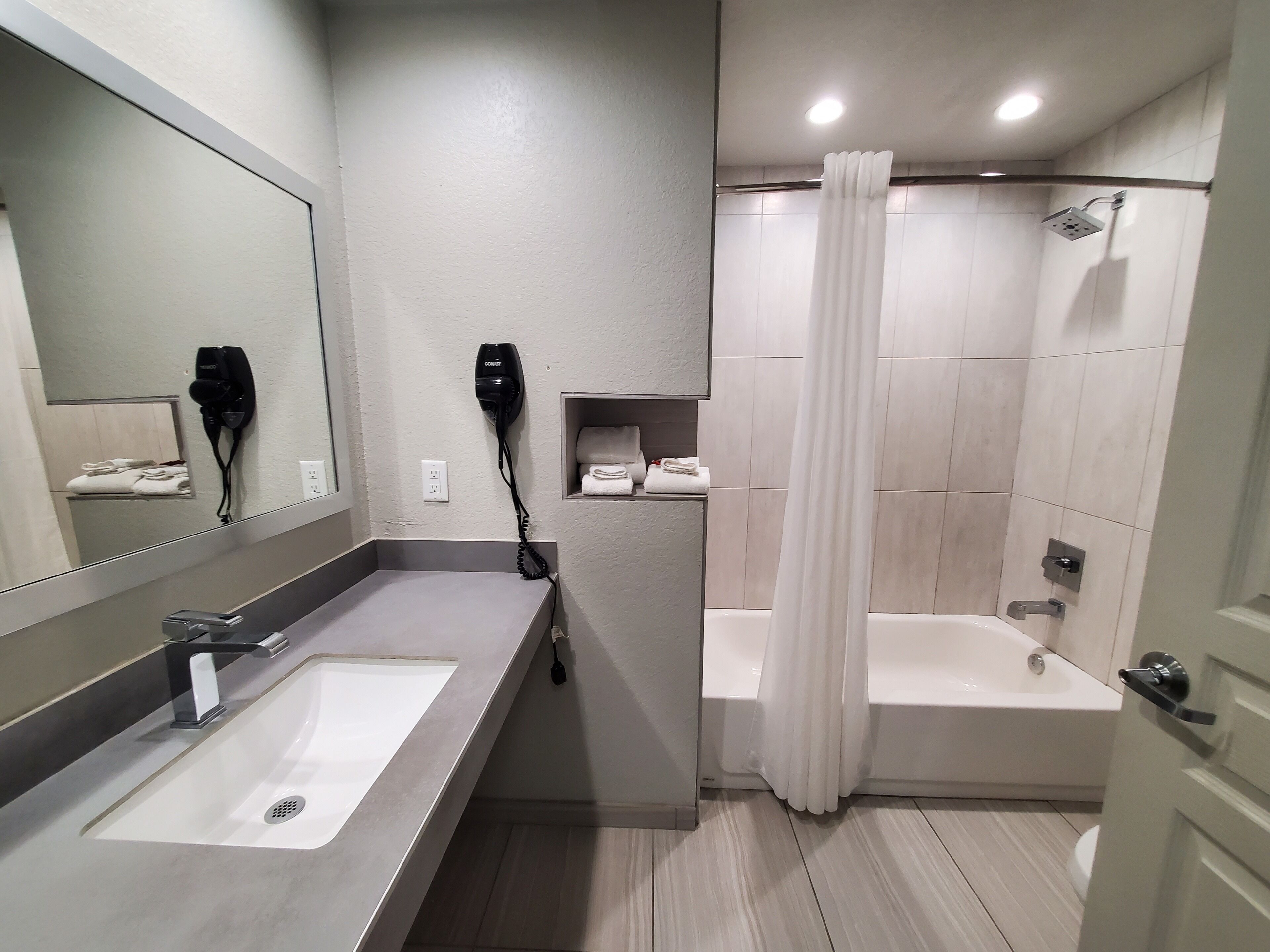 A modern bathroom with a sink, a hairdryer, a shower, and a bathtub.
