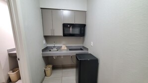 Una cocina pequeña con un lavamanos, un microondas, armarios y un cubo de basura.