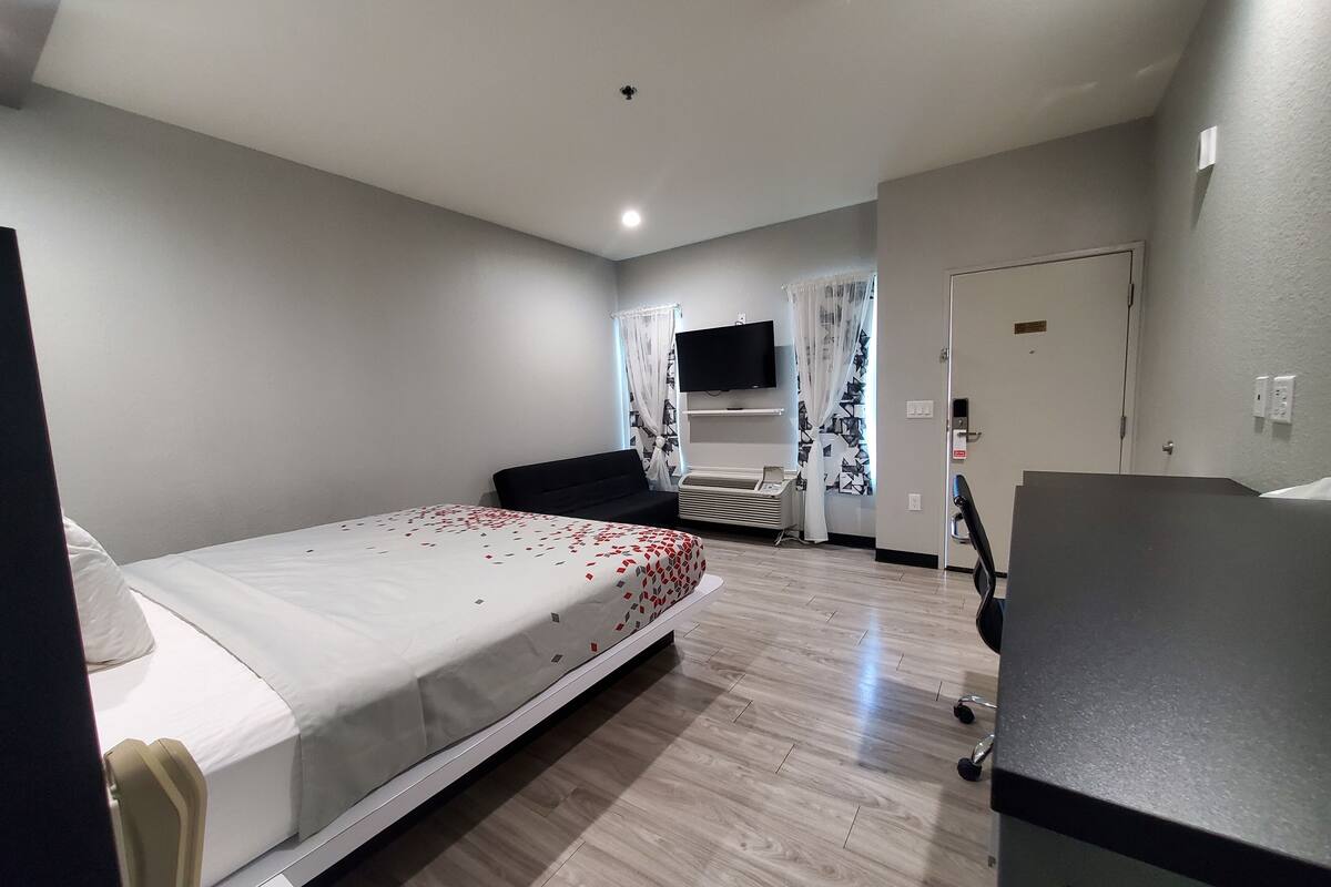 A hotel room with a bed, a desk, a chair, a TV, and a door.