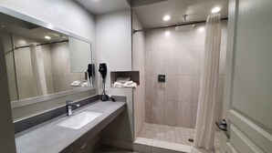 Un baño moderno con un espejo grande, un lavamanos, una ducha y un perchero para toallas.