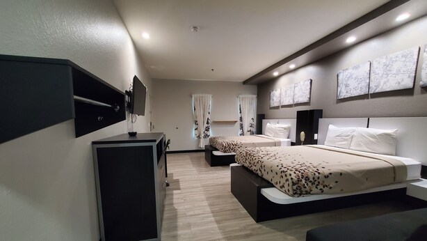 Una habitación de hotel moderna con escritorio, dos camas, un sofá y obras de arte en las paredes.