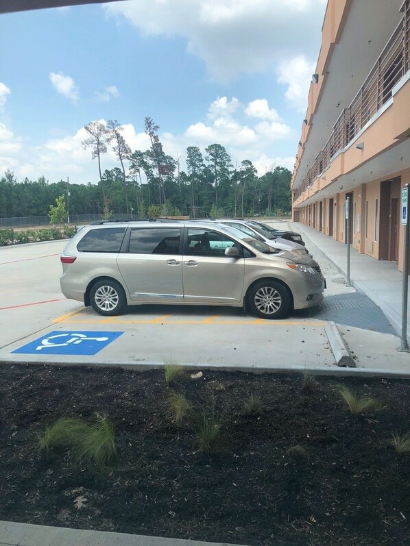 Un espace de stationnement avec un panneau indiquant les places réservées aux personnes handicapées, un monospace beige et un bâtiment doté de plusieurs portes.