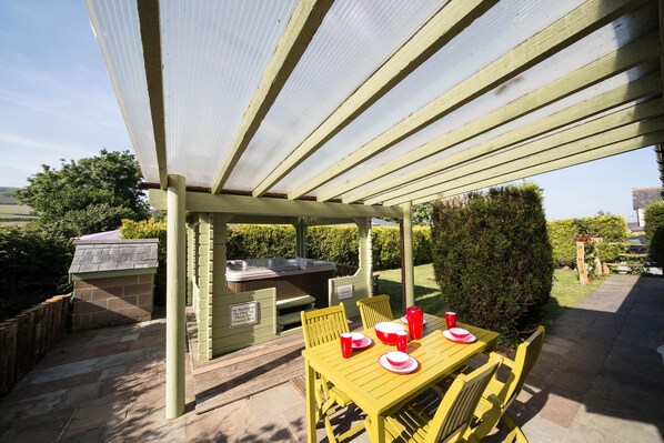 Un patio exterior con zona de estar cubierta, una parrilla y un jacuzzi.