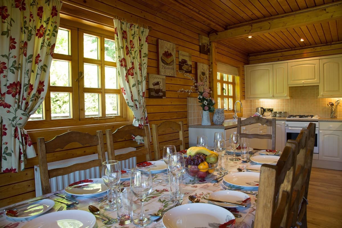 A wooden cabin with a dining area set for a meal, featuring a table with plates, cutlery, and a fruit bowl.
