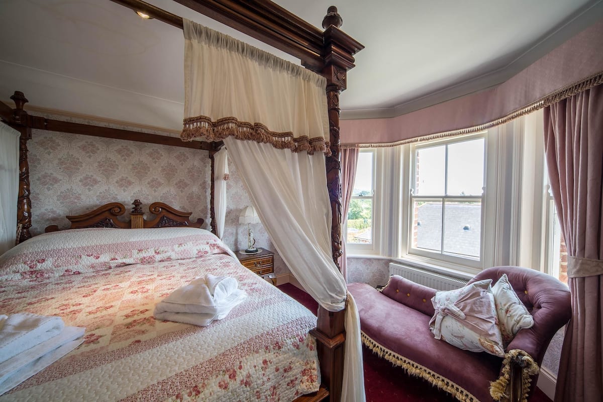 A four-poster bed with a canopy, a plush sofa, and a large window with curtains.