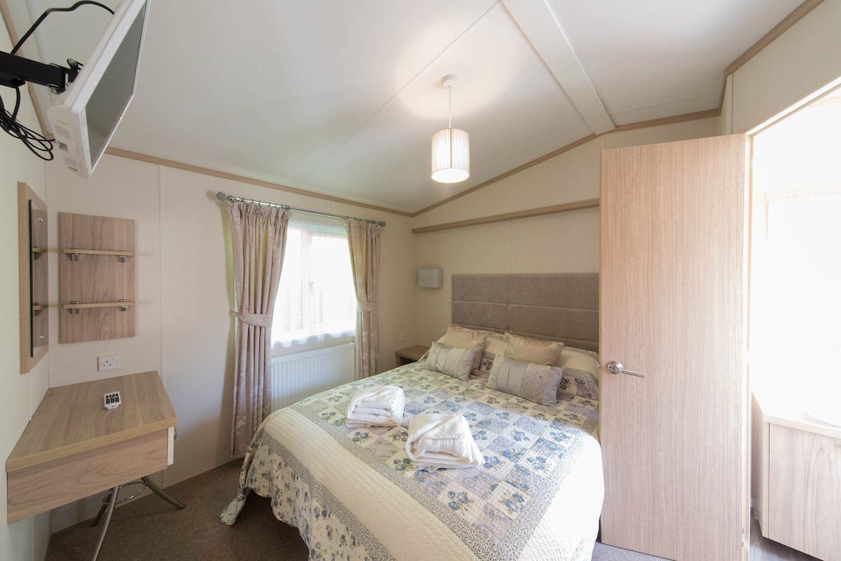 A bedroom with a bed, a desk, a wardrobe, a window with curtains, and a ceiling light.