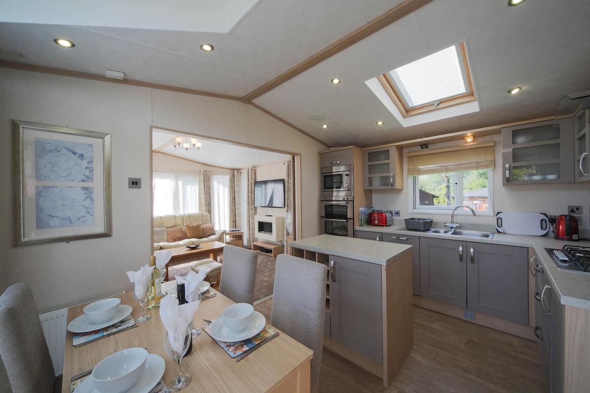 A modern kitchen with a dining area, featuring a skylight, built-in appliances, and a view of the outdoors.