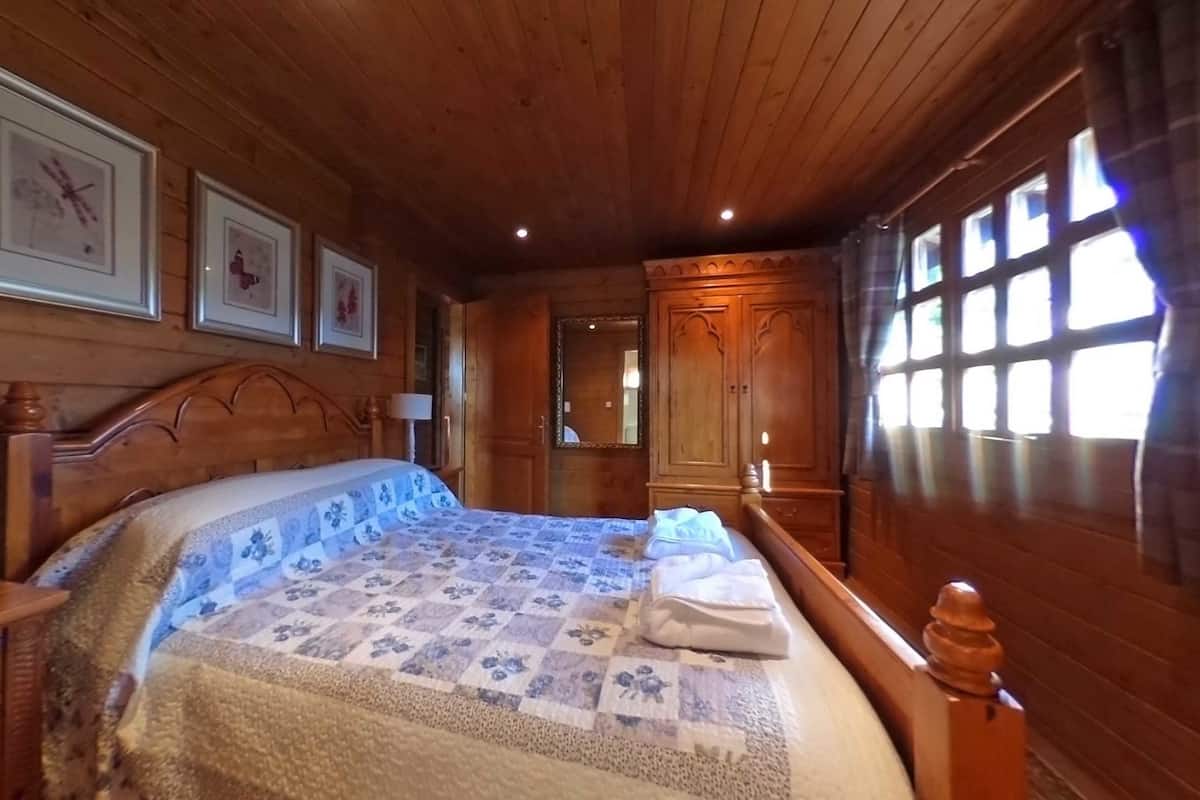 A wooden-paneled bedroom with a bed, a wardrobe, and framed pictures on the wall.