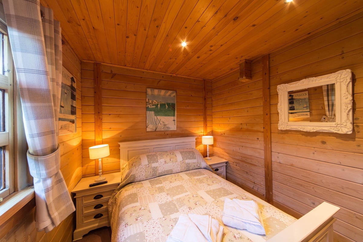A wooden cabin room with a bed, two bedside tables, a lamp, and a painting on the wall.