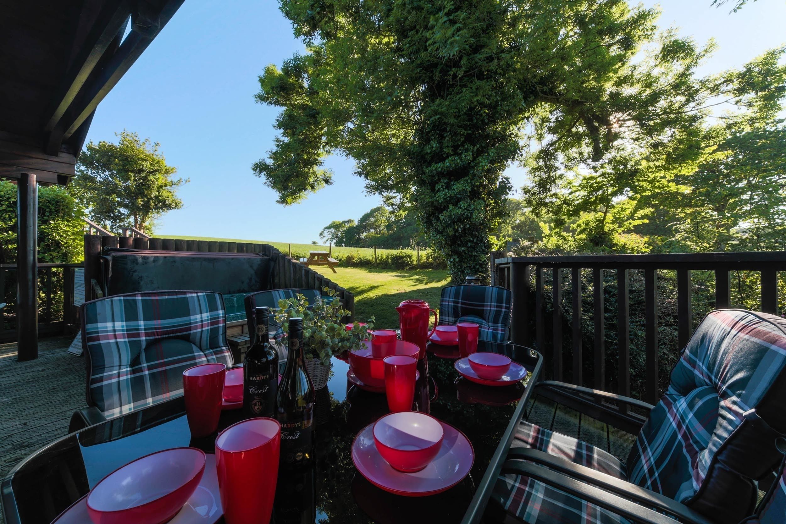 An outdoor seating area with plaid furniture and red tableware, overlooking a grassy landscape.