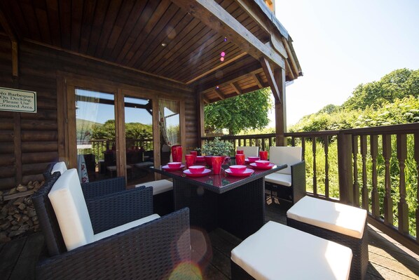 An outdoor wooden deck with a table set for dining, wicker furniture, and a sign prohibiting barbecues.