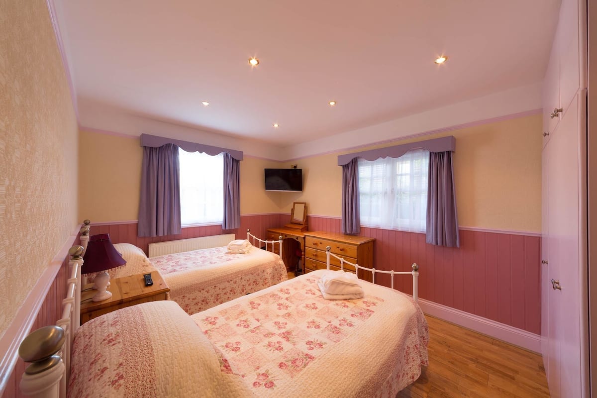 A bedroom with two beds, a dresser, a TV, and a window with curtains.
