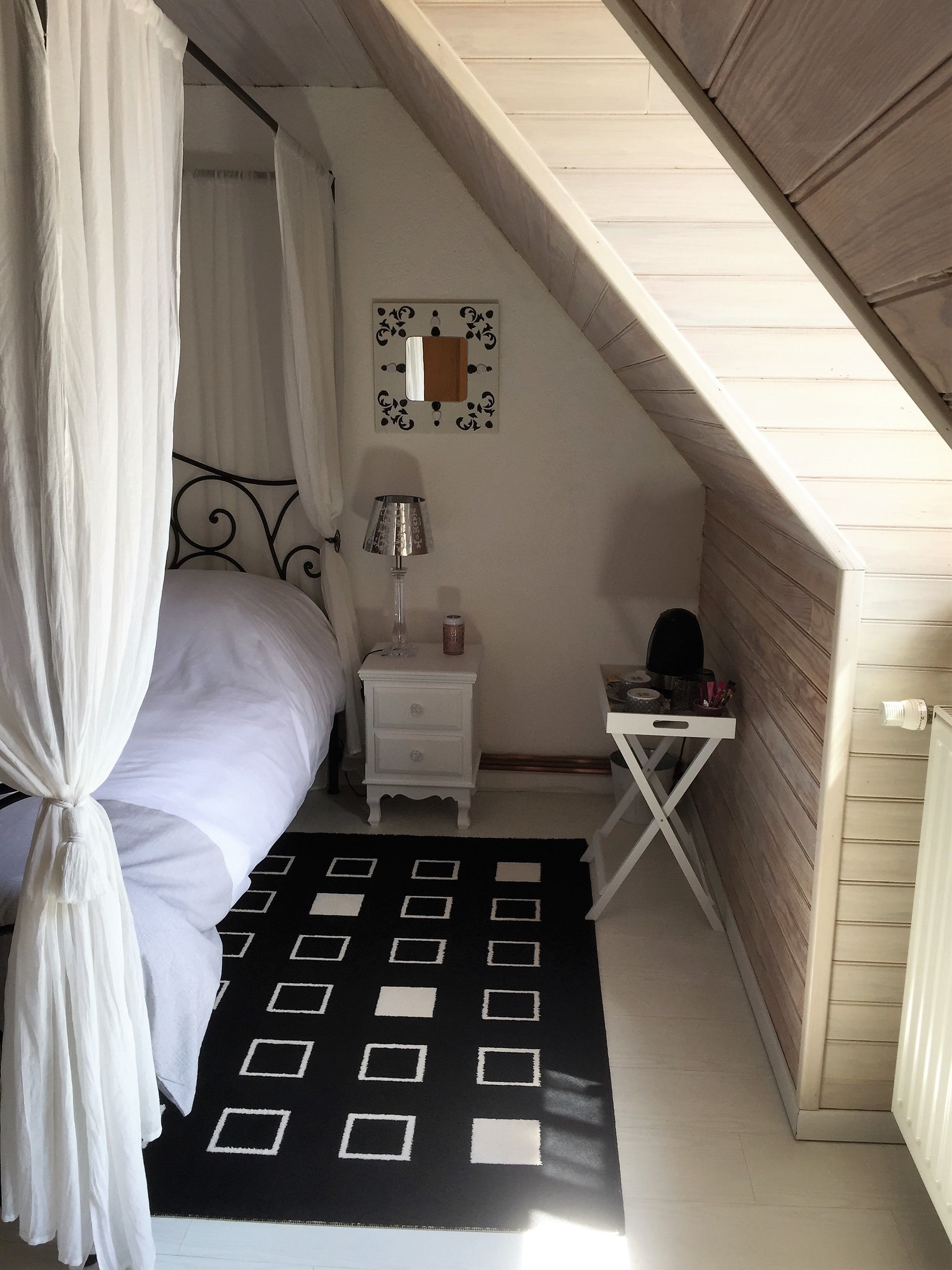 Une chambre à coucher avec un lit à baldaquin, une table de chevet avec une lampe, un petit bureau et un tapis à motifs.