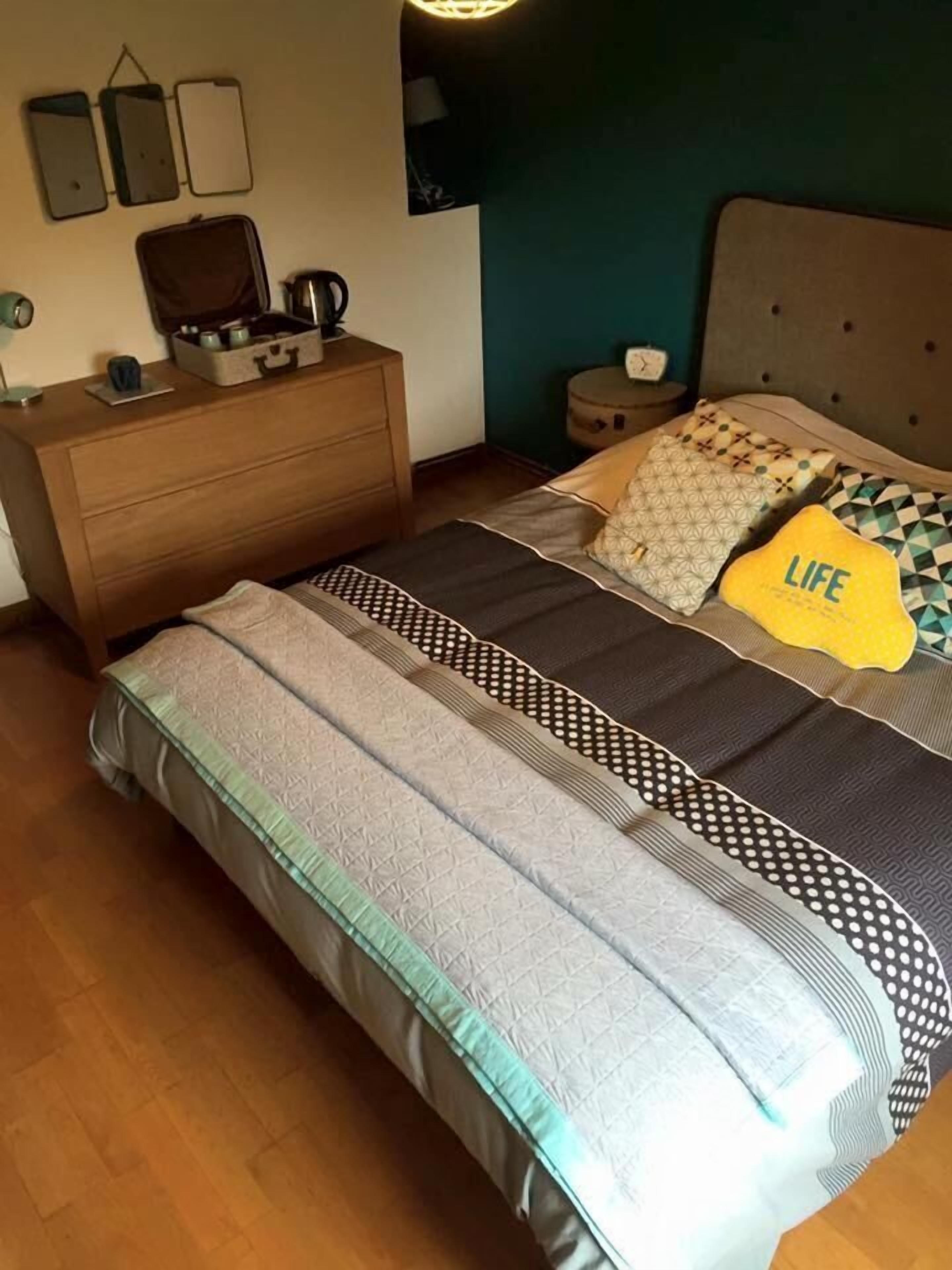 A bedroom with a bed, a dresser, a nightstand, and a wall-mounted shelf.