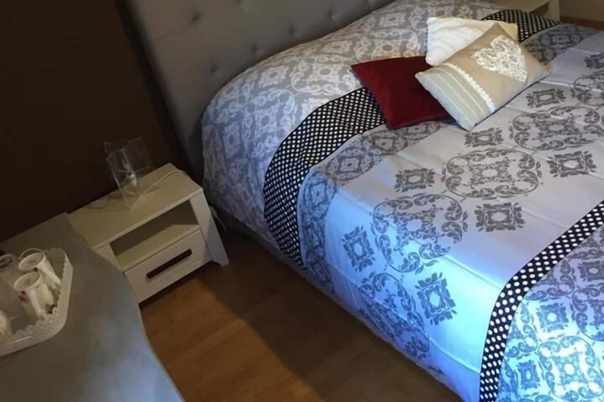 Quarto com cabeceira estofada, roupa de cama estampada e um objeto decorativo na parede.