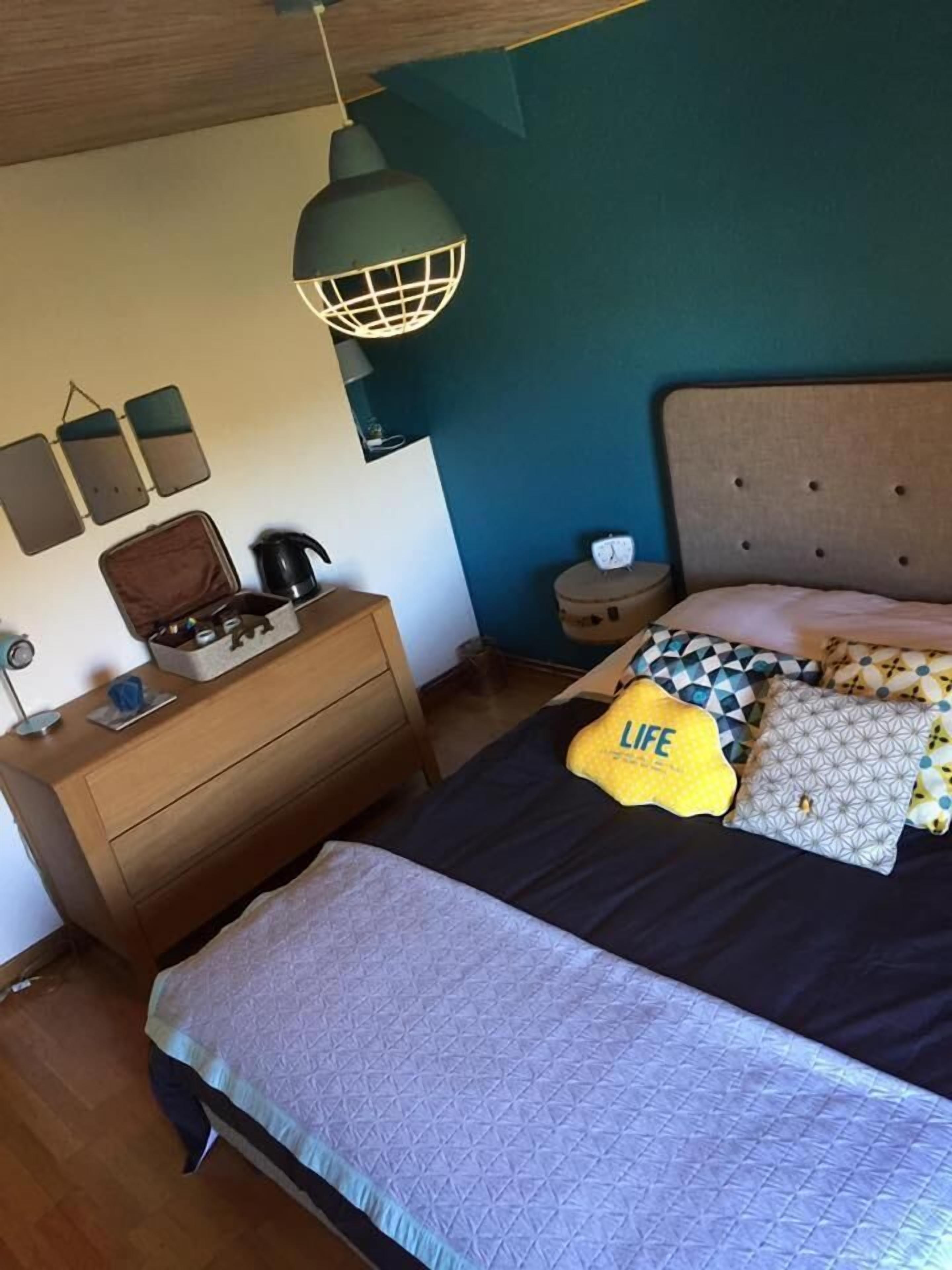 A bedroom with a bed, bedside table, dresser, lamp, and wall decorations.