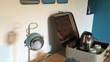 Et træskrivebord med en vintage lampe, en lille bakke med en blå genstand, og en læderindbundet mappe med et metal krus og en termokande.