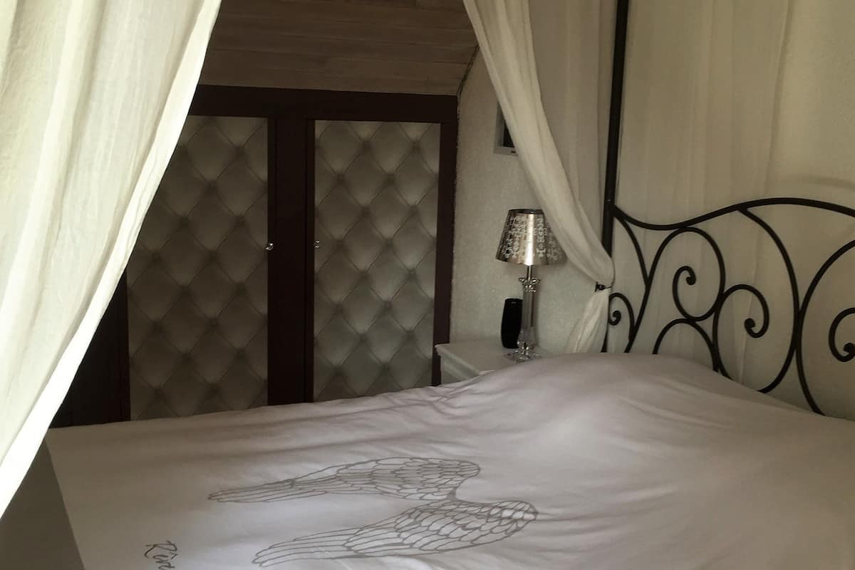 Uma cama com dossel branco, cabeceira estofada e mesa de cabeceira com abajur.
