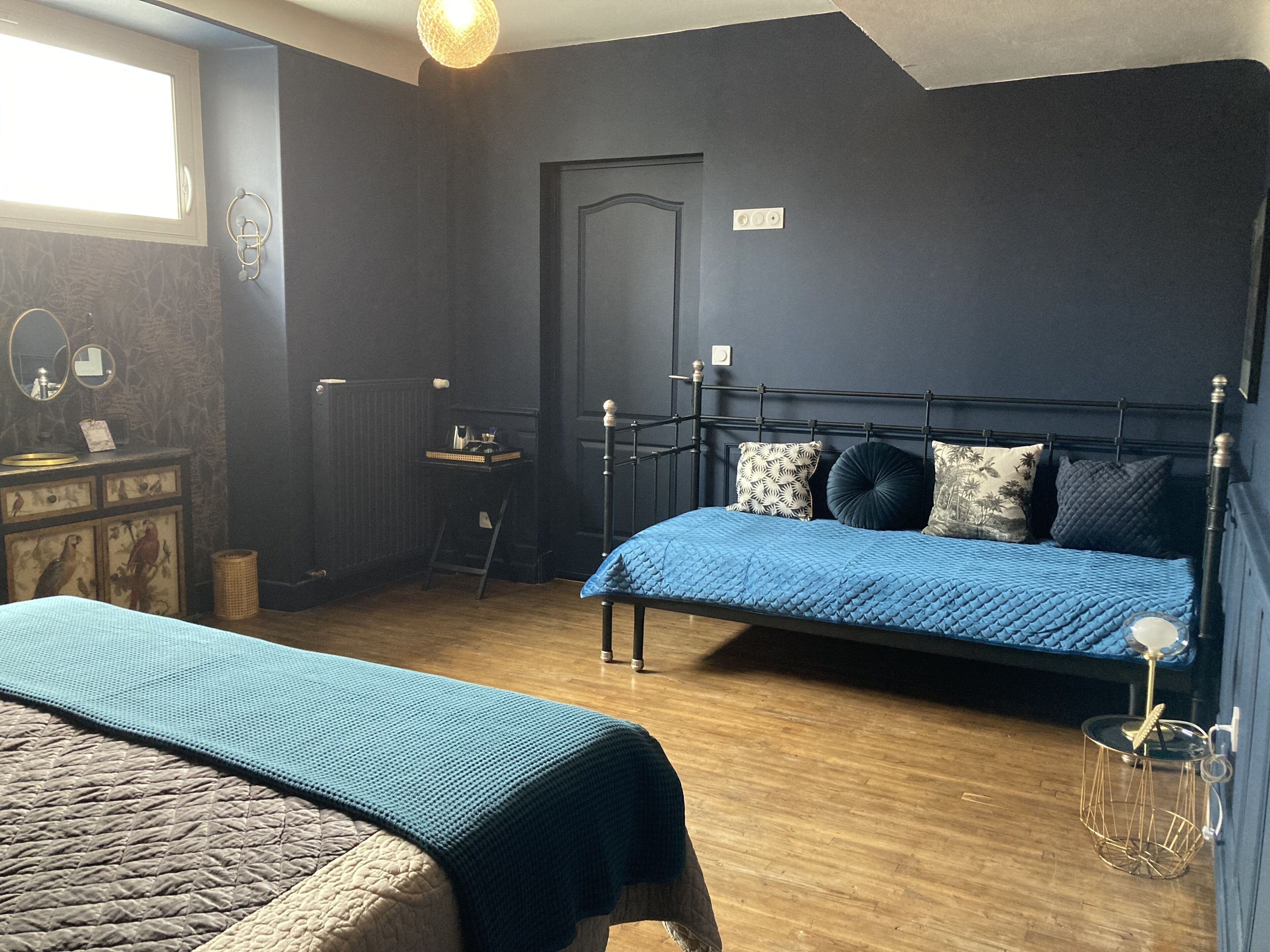 Ein Schlafzimmer mit einem großen Bett, einem kleineren Bett, einem Schminktisch und einem Spiegel sowie einem Fenster.