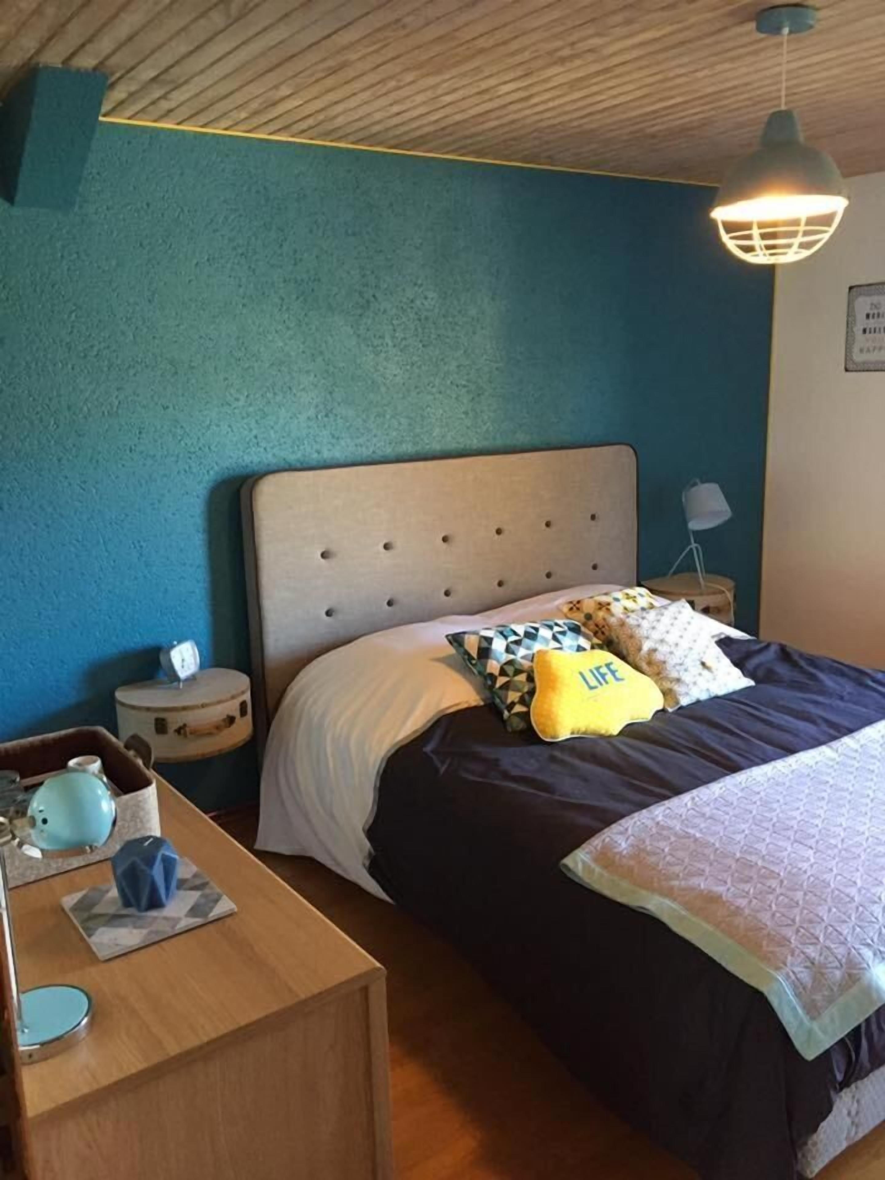 Un dormitorio con una cama, una mesita de noche de madera, una lámpara y una pequeña mesa con una tetera y tazas.