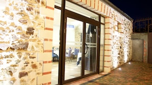 A stone building with a glass door entrance, a brick wall, and a tiled patio area. - Hôtel Auberge de la Loire (Mauges-sur-Loire)
